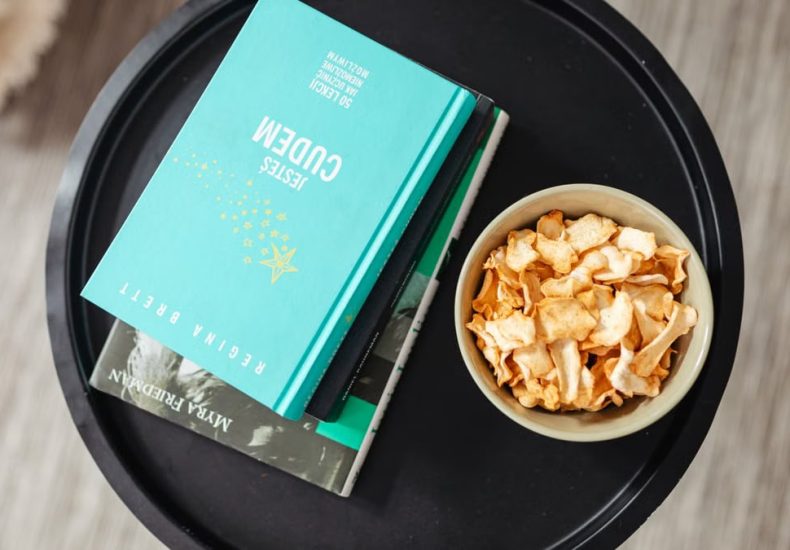 Aerial view of a stack of books and a snack bowl on a round table, creating a cozy reading nook.